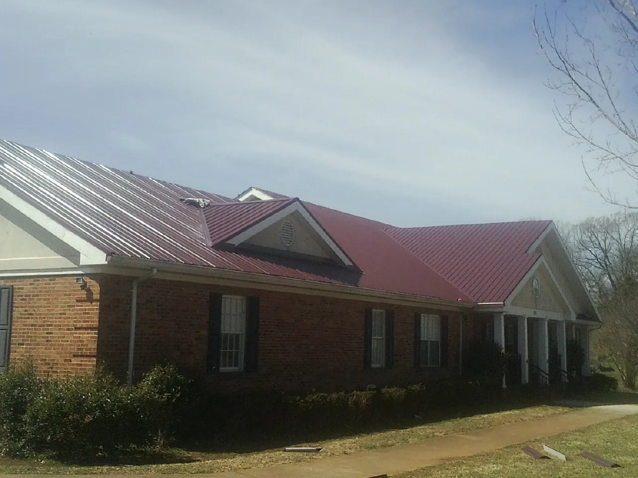 Red metal roof with gabled entries on a long brick building, from a Hail Damage Roof Repair job in Beacon